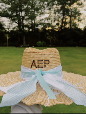 A straw hat with AEP monogram and teal ribbon
