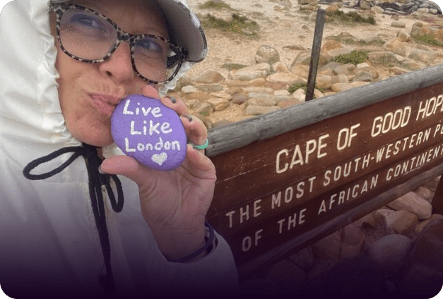 A Live Like London purple rock held up at the Cape of Good Hope sign — the most south-western point of the African continent.